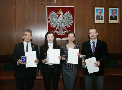 prof. dr hab inż. Józef Dziopak, mgr inż. Agnieszka Stec, mgr inż. Joanna Hypiak, dr inż. Daniel Słyś trzymając dyplomy w sali. W tle widać godło Polski.